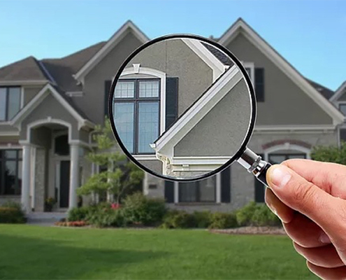 A hand holding a magnifying glass in front of a suburban home to signify an inspection